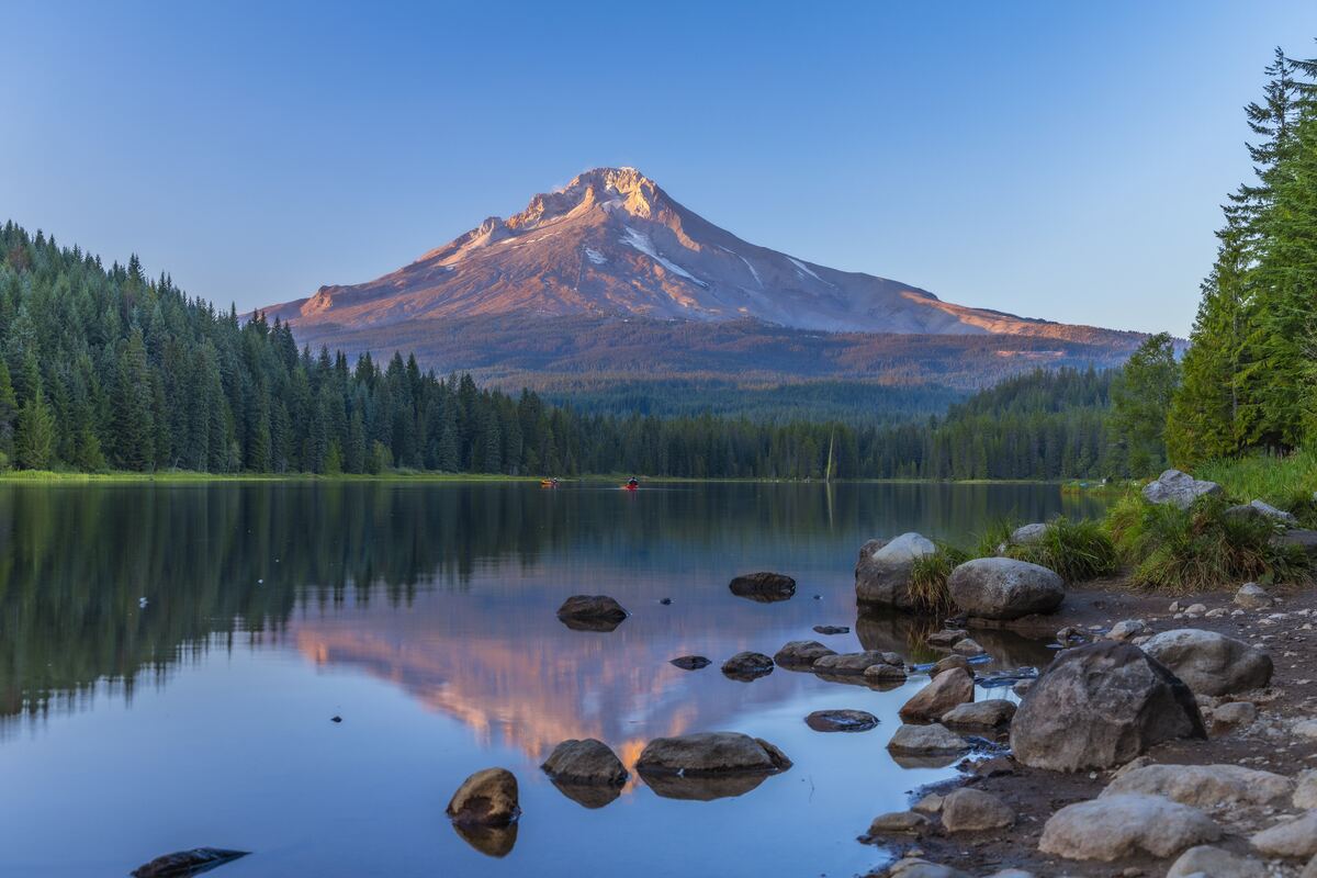 Mountain lake reflecting first light at dawn, still water and forest.